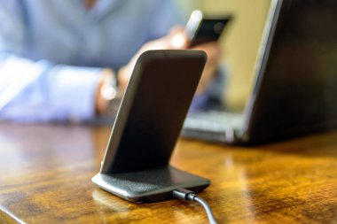 Kablosuz telefon şarjı. Ofiste elinde akıllı telefon olan bir adam var.