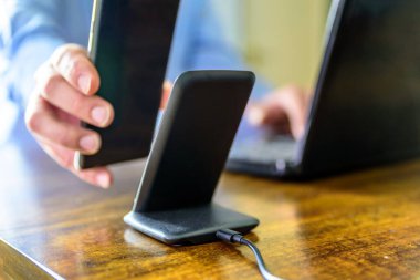 Adam akıllı telefonu kablosuz şarj cihazıyla şarj ediyor.