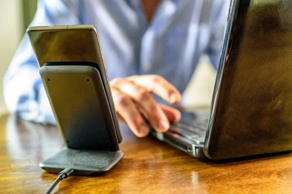 Carregamento de telefone sem fio stand sobre o homem que trabalha no laptop no escritório em casa — Fotografia de Stock
