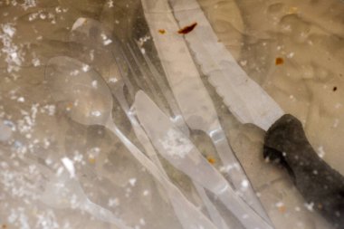 Kirli çatal bıçak ve kaşık, mutfak lavabosunun içindeki suyun altında kremayla kaplı.