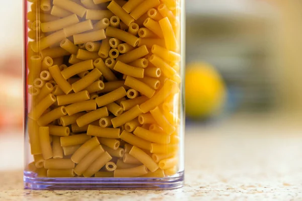 Raw italian macaroni pasta inside clear storage container — Stock Photo, Image