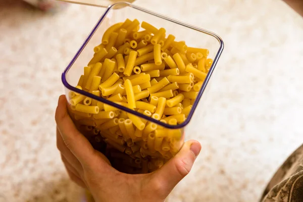 Enfants mains ouverture pâtes macaroni à l'intérieur récipient de rangement clair sur plan de travail de cuisine — Photo