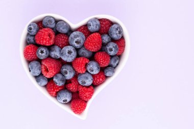 Yaban mersini ve ahududu, kalp şeklinde bir tabakta meyve porselen bir çanakta pastel arka planda