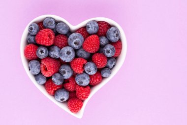 Yaban mersini ve ahududu, kalp şeklinde bir tabakta meyve porselen bir çanakta pastel arka planda