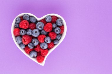 Yaban mersini ve ahududu, kalp şeklinde bir tabakta meyve porselen bir çanakta pastel arka planda