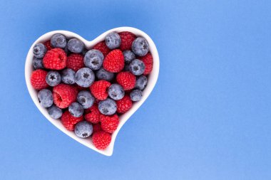 Yaban mersini ve ahududu, kalp şeklinde bir tabakta meyve porselen bir çanakta pastel arka planda