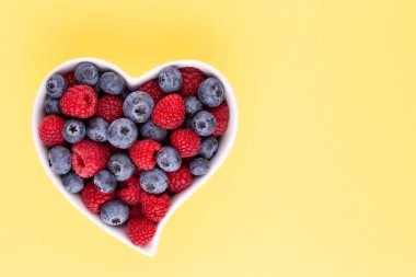 Yaban mersini ve ahududu, kalp şeklinde bir tabakta meyve porselen bir çanakta pastel arka planda