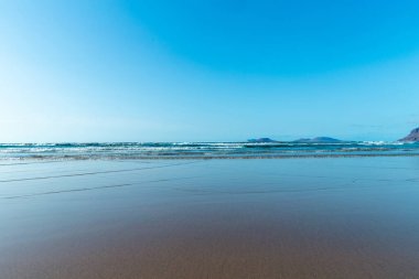 Güzel sahil manzarası ve tropikal Lanzarote denizi. Kanaryalar. Famara Sahili, Lanzarote Adası, Kanarya Adaları. Lanzarote adasındaki en popüler plajda turistler.