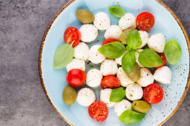 Kiraz domatesleri, mozzarella peyniri, fesleğen ve baharatlar gri tahta üzerinde. İtalyan geleneksel Caprese salata malzemeleri. Akdeniz yemekleri.