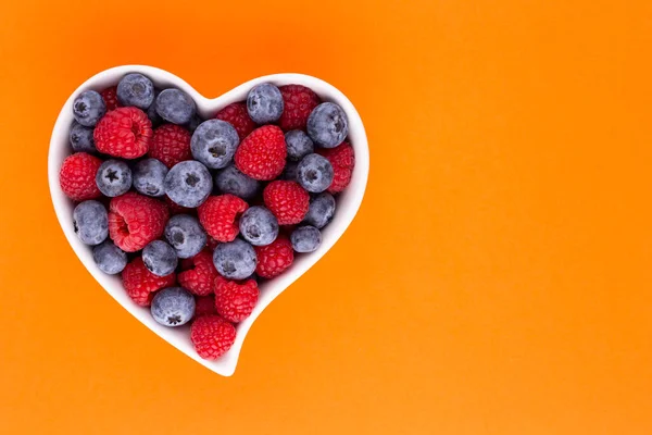Blueberry and raspberries, fruit in a heart shaped dish on a porcelain bowl pastel background