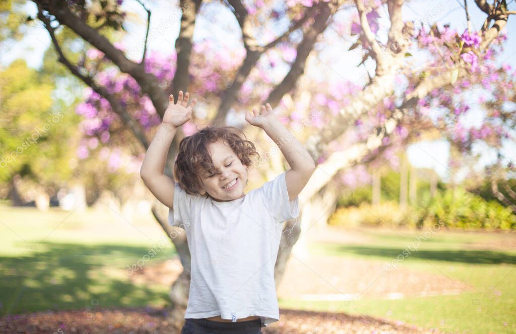 child outdoors in a sunny day, happy put his hands up in the air