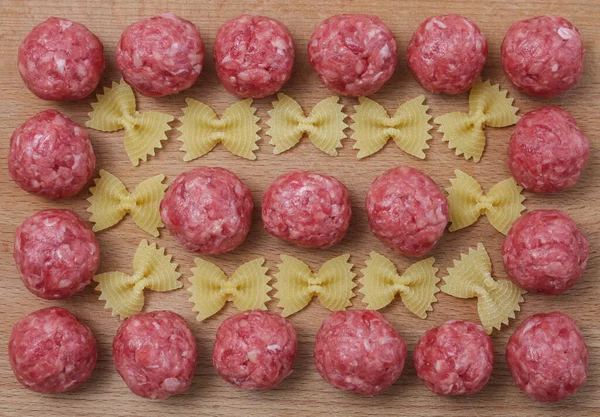 Raw meatballs and pasta bows on a wooden Board. — Stock Photo, Image