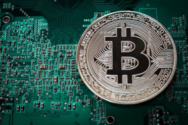 Yeşil baskılı devre kartında gümüş bir bitcoin yatıyor..