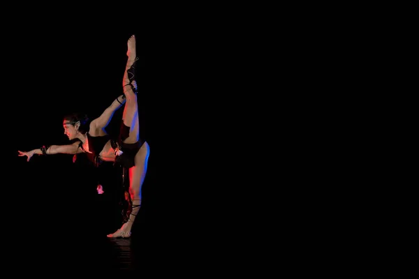 woman athlete gymnast in the form of an elf performs acrobatics on a black background in the scenic red and blue light.