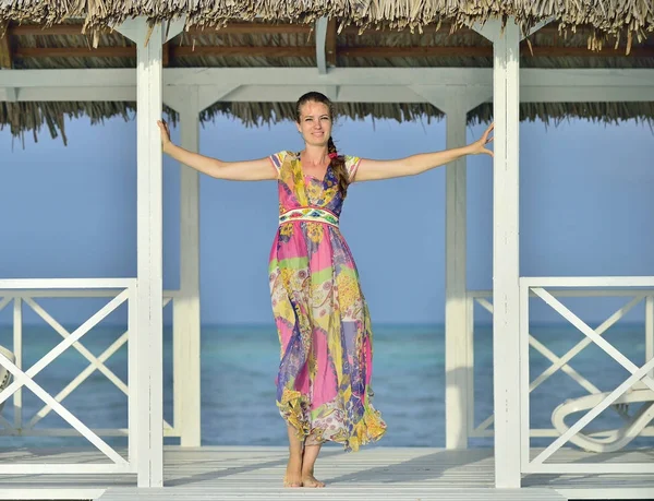 在古巴海滩的白色木码头上 一个穿着彩色连衣裙的微笑的女孩 在假期里看起来很开心很放松 — 图库照片