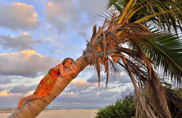 小女孩在热带海滩坐在棕榈树在暑假期间 夕阳灯 — 图库照片