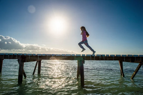 日の出に木製の桟橋で実行している少女のシルエット 太陽を背景に 澄んだ海 青い空 早朝だ キューバだ ココ島 — ストック写真