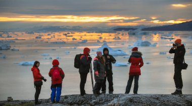 RODEBAY, BATI GREENLAND, 11 Temmuz 2018. Rodebay 'deki buzdağlarına bakan bir grup insan, Oqaatsut olarak da bilinir. Rodebay dağından gelen buzdağlarıyla Disco Körfezi manzarası. Gün batımı görünümü. 