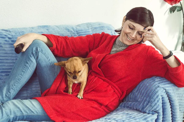 Çekici, gülümseyen bir kadın kanepeye uzanmış köpeğiyle oturuyor. 