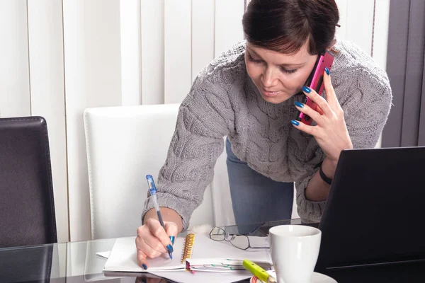 Business woman taking notes while talking on the smart phone — ストック写真