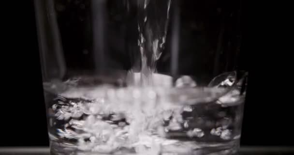 Человек наливает стакан воды на черный фон — стоковое видео