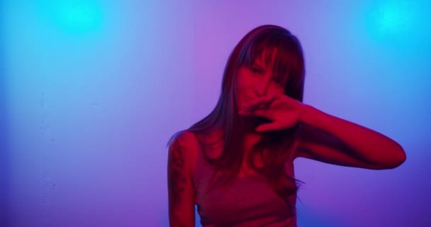 Turns to the camera and looks and smiles, cute looks in neon light — ストック動画