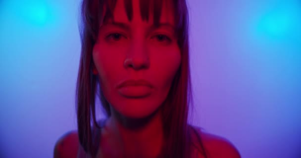 Turns to the camera and looks and smiles, cute looks in neon light — Stockvideo