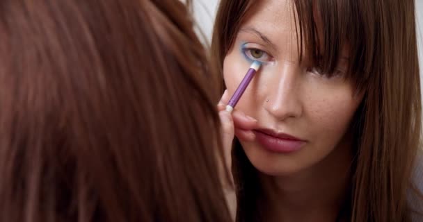 Professionell makeup artist gör makeup av ung modell. Närbild av make-up konstnärens hand applicera ögonskugga med speciell borste till ung kvinna för att delta i modevisning. Skönhet och mode — Stockvideo