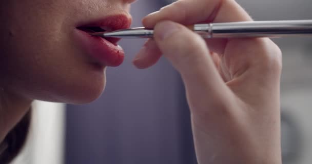 Maquilladora trabaja con la modelo, aplica lápiz labial con un pincel en los labios de la modelo, primer plano macro. pinta los labios . — Vídeo de stock