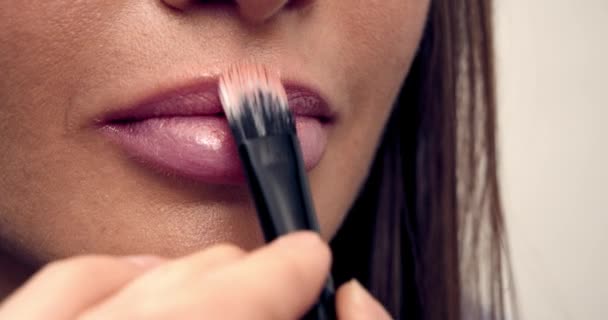 Maquilladora trabaja con la modelo, aplica lápiz labial con un pincel en los labios de la modelo, primer plano macro. pinta los labios . — Vídeo de stock