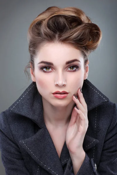 Porträtt av eleganta ung kvinna i en grå överrock på grå bakgrund — Stockfoto
