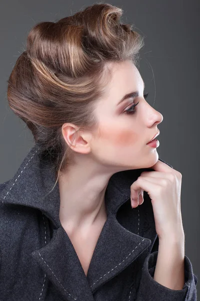 Portret van elegante jonge vrouw in een grijze overjas op een grijze achtergrond — Stockfoto