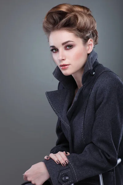 Szürke háttéren egy szürke felöltő-elegáns fiatal nő portréja — Stock Fotó