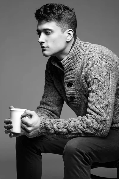 Jovem sexy em camisola de malha quente com uma xícara de chá em suas mãos. Modelo masculino . — Fotografia de Stock