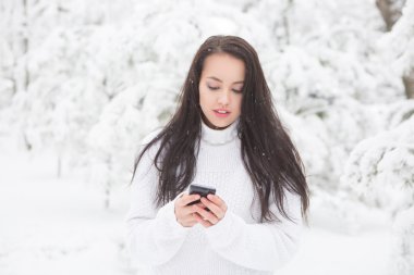 Akıllı telefon ve kış manzarası ile gülümseyen genç kadın