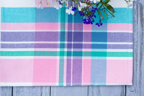 Close up on checkered tablecloth fabric. pink, green, violet with white tartan square pattern with blooming lobelia — Stock Photo, Image