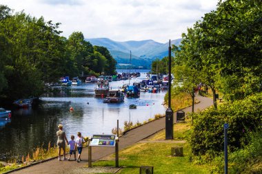 Lomond Gölü yakınlarındaki Balloch limanının manzarası. Leven nehrinde tekneler ve İskoçya 'da güneşli bir günde yürüyen ve dinlenen turistler..