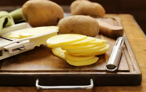 Patatas crudas peladas y cortadas en rodajas en una tabla de cortar — Foto de Stock