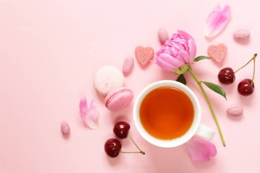 Bir fincan çay bir kadın, acıbadem kurabiyesi, çiçekler ve pembe bir arka plan üzerinde tatlılar için