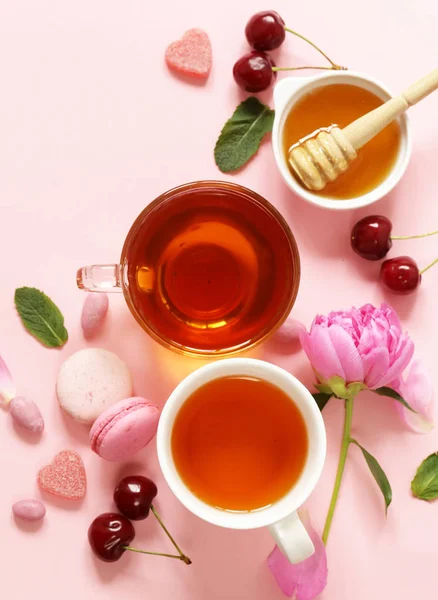 Een kopje thee voor een vrouw, macaroon, bloemen en snoep op een roze achtergrond — Stockfoto