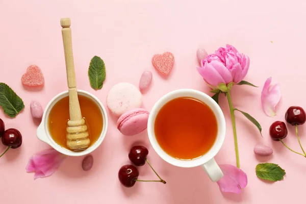 Een kopje thee voor een vrouw, macaroon, bloemen en snoep op een roze achtergrond — Stockfoto