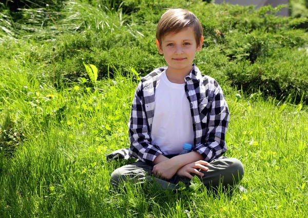 Sevimli sarışın çocuk yeşil çimenlerin üzerinde oturuyor — Stok fotoğraf