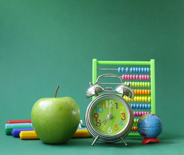 Школьная канцелярия и яблоко на зеленом фоне — стоковое фото
