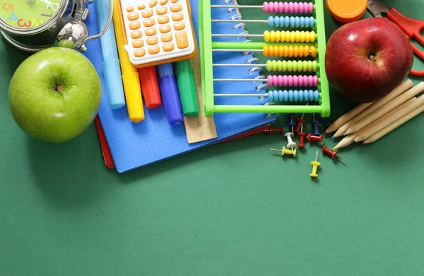 Школьные принадлежности и яблоко на зеленом фоне — стоковое фото