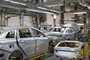 Russia, Izhevsk - December 14, 2019: LADA Automobile Plant Izhevsk. The worker is setting motor hood on a new car. clipart