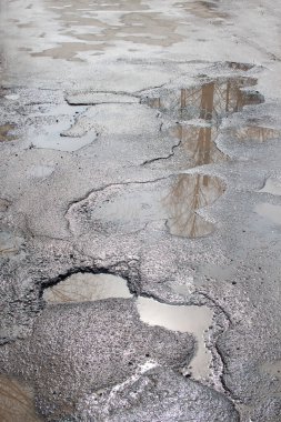 Tehlikeli yol yatağı yok edildi. Kötü asfalt yol. Suyla dolu büyük bir çukur. Sudaki yansıma ışınları..