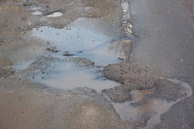 Çukur suyla dolu, asfalt bir yol. Tehlikeli yol yatağı yok edildi. Su birikintisindeki temiz su.