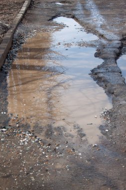Tehlikeli yol yatağı yok edildi. Büyük bir çukur ve suyla dolu kötü asfalt yol. Sudaki ayna yansıma ağaçları.
