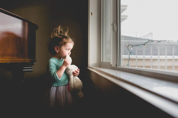 Маленькая девочка в платье смотрит в окно — стоковое фото