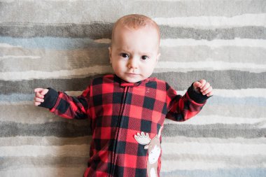 Kırmızı ekose uyuyan sevimli bebek çocuk arkasında uzanır ve kamera için yüz yapıyor